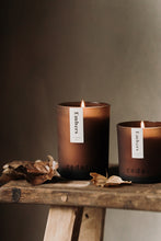 Load image into Gallery viewer, Embers essential oil candles in an amber glass jar. Both small and large candles are sat on a bench with a few leaves